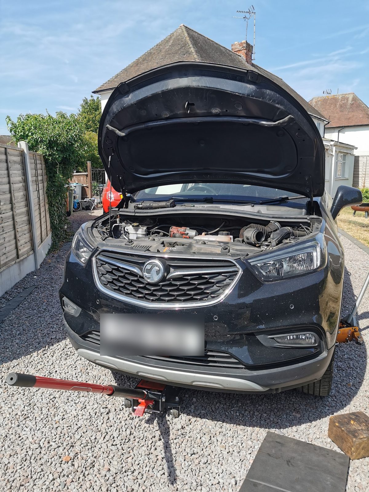 Black Vauxhall Mokka on a gravel driveway with the bonnet open and a trolley jack in front