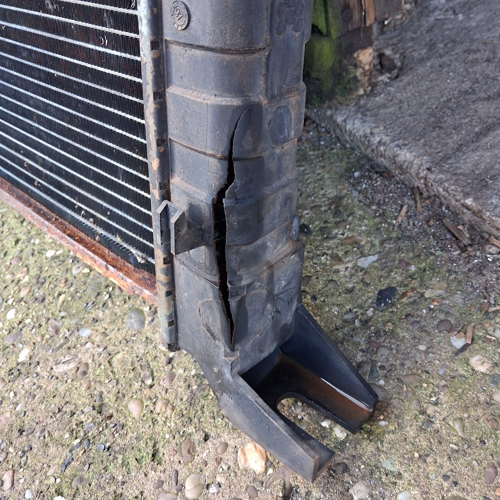 A worn, split rubber hose removed from a car, laid on gravel