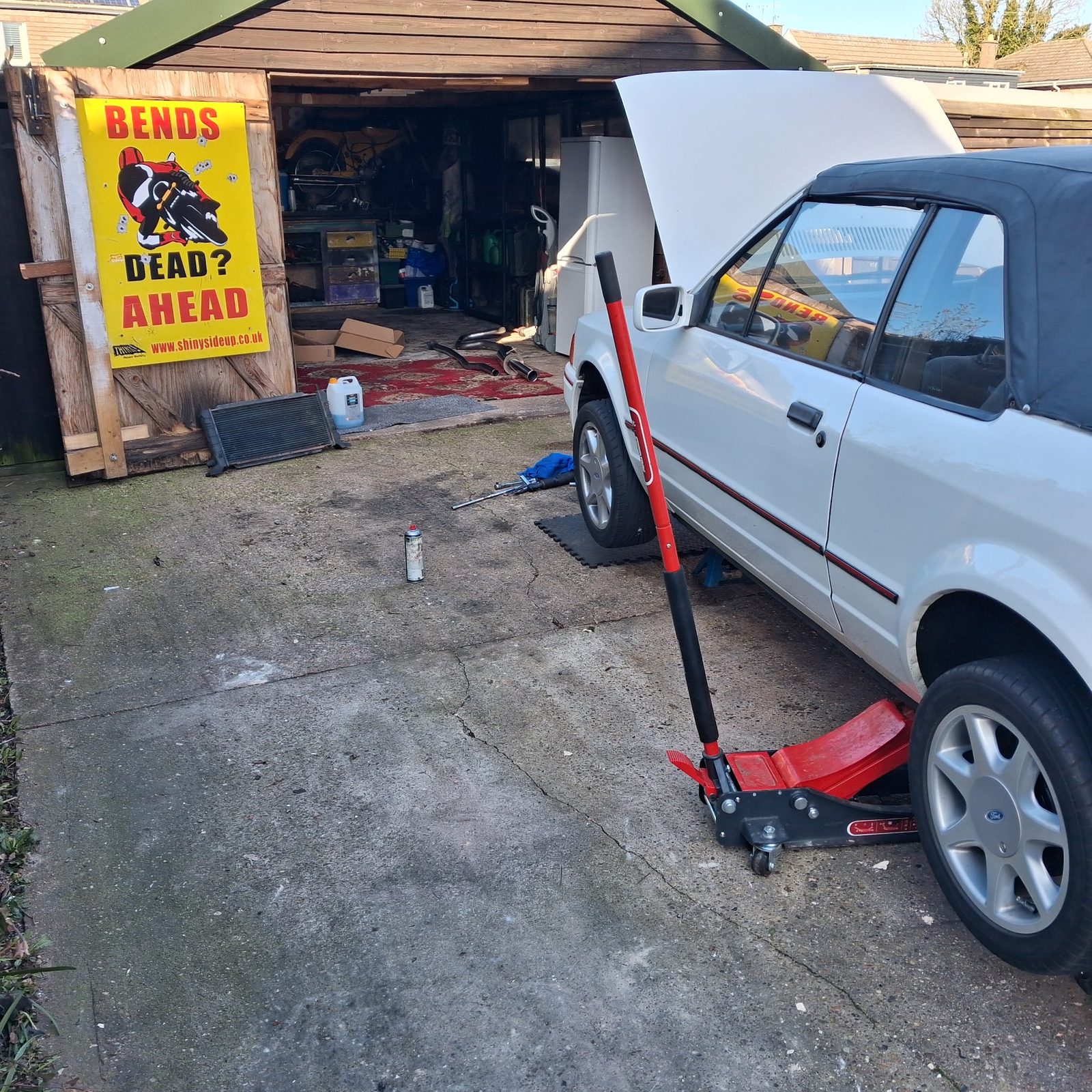 White Ford Escort XR3i cabriolet raised on a trolley jack outside a garage