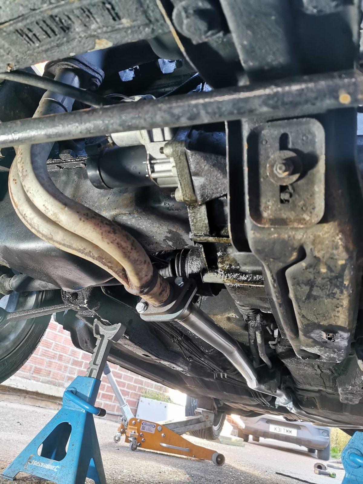 Underneath a car on axle stands, exhaust and subframe in view